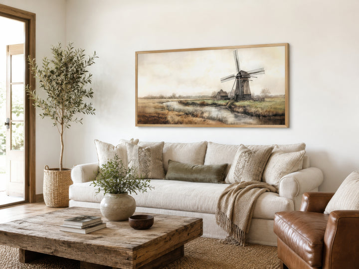 Vintage windmill canvas print in a light wood frame hanging above a neutral sofa in a rustic room.