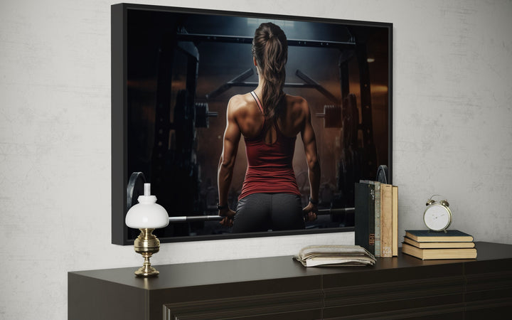 Motivational gym wall art featuring a strong woman lifting a barbell on a framed canvas.