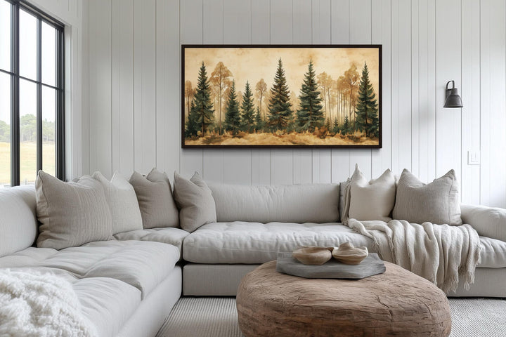 a cozy living room with a large, comfortable sectional sofa adorned with throw pillows. Above the sofa, a framed painting of a forest scene hangs on the wall, adding a touch of nature to the space. The room is further decorated with a wooden coffee table and a lamp, creating a warm and inviting atmosphere.