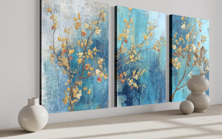 Three-panel canvas wall art featuring gold blossoms on a textured blue and grey background.