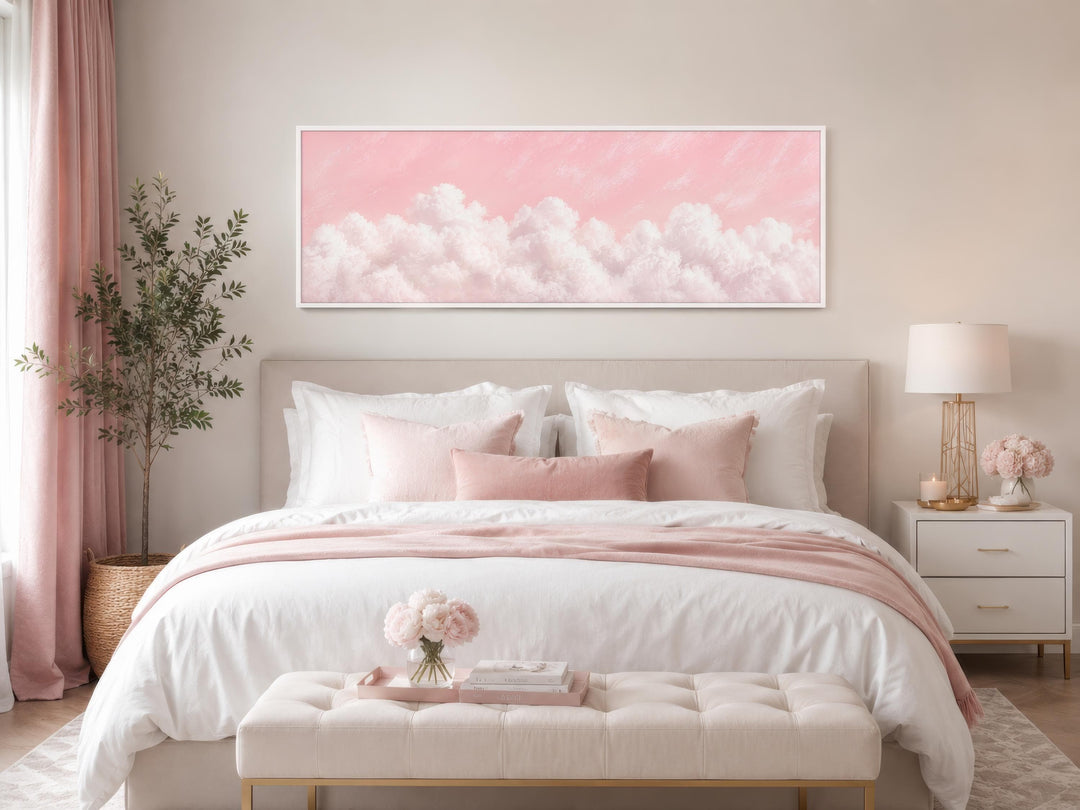 Long horizontal canvas print of fluffy white clouds on a blush pink sky above a bed.