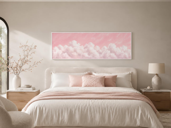 Fluffy white clouds on a blush pink sky long horizontal canvas print above a bed in a soft bedroom.