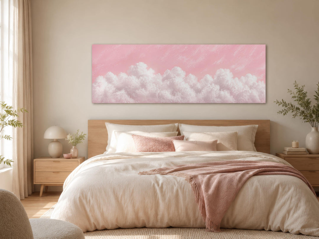 Fluffy white clouds on a blush pink sky long horizontal canvas print hanging above a bed.