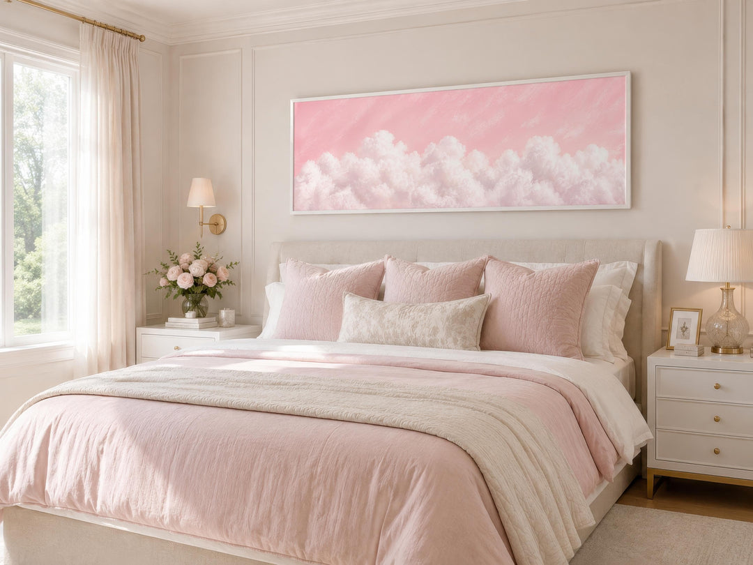 Fluffy white clouds on a blush pink sky long horizontal canvas print hanging above a bed.