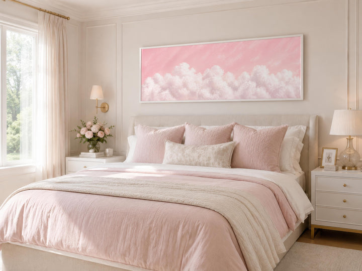 Fluffy white clouds on a blush pink sky long horizontal canvas print hanging above a bed.