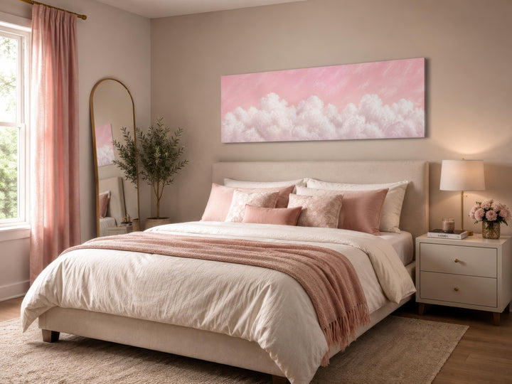 Long horizontal canvas print of fluffy white clouds on a blush pink sky above a neutral bed.