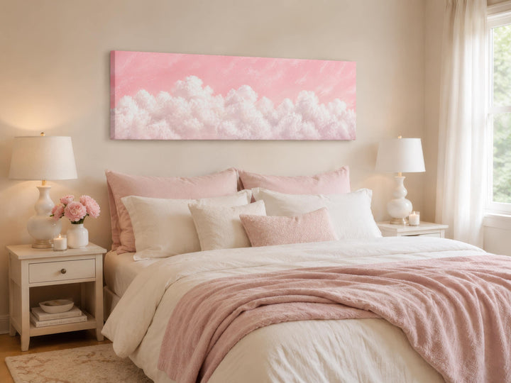 Long horizontal canvas print of fluffy white clouds on a blush pink sky above a bed.