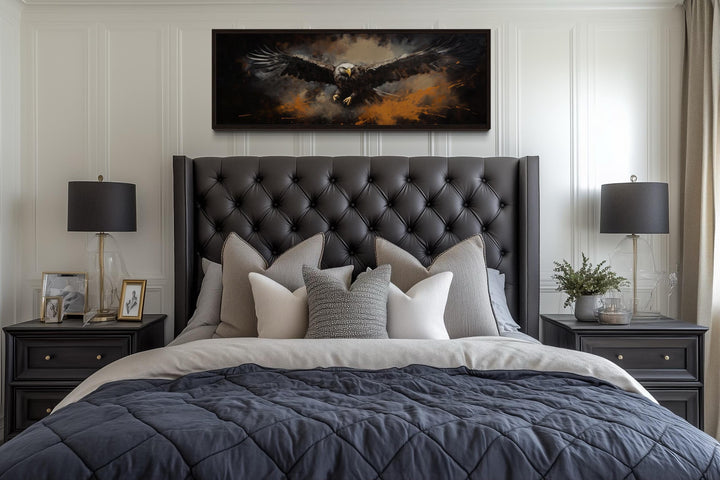 Long horizontal canvas art of a bald eagle in flight above a tufted headboard in a bedroom.