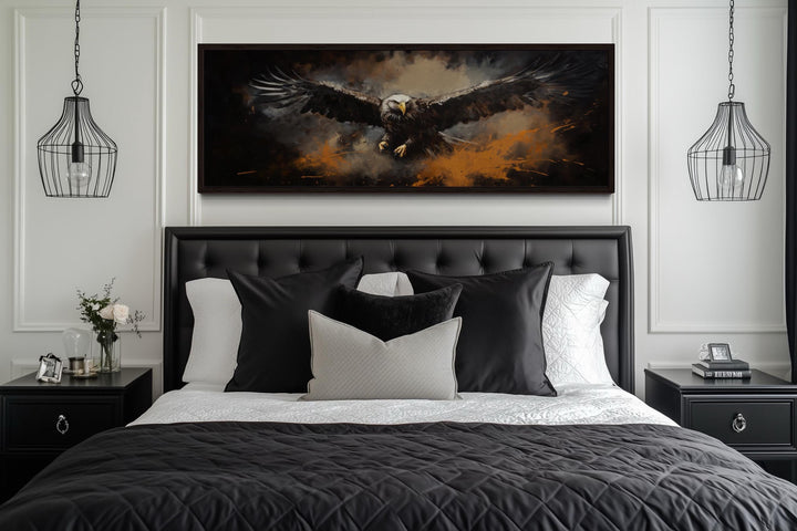 A long horizontal canvas of a bald eagle in flight above a black tufted headboard in a bedroom.