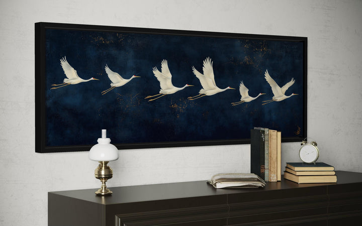 Panoramic wall art of white cranes flying across a deep navy blue background in a black frame.
