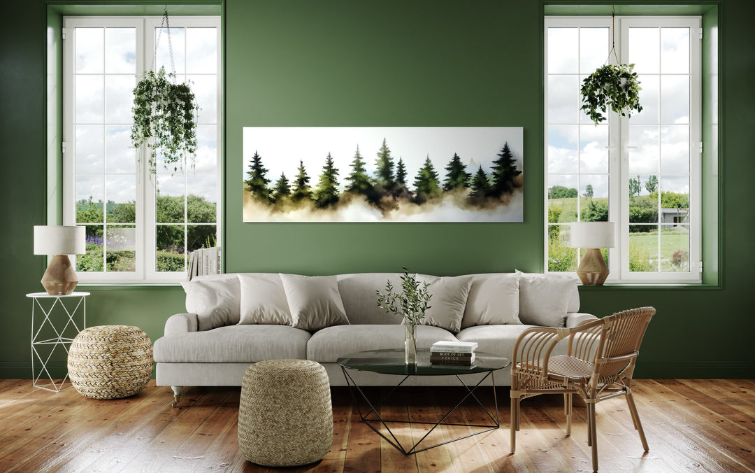 Panoramic watercolor wall art of foggy green pine trees hanging above a sofa in a green room.