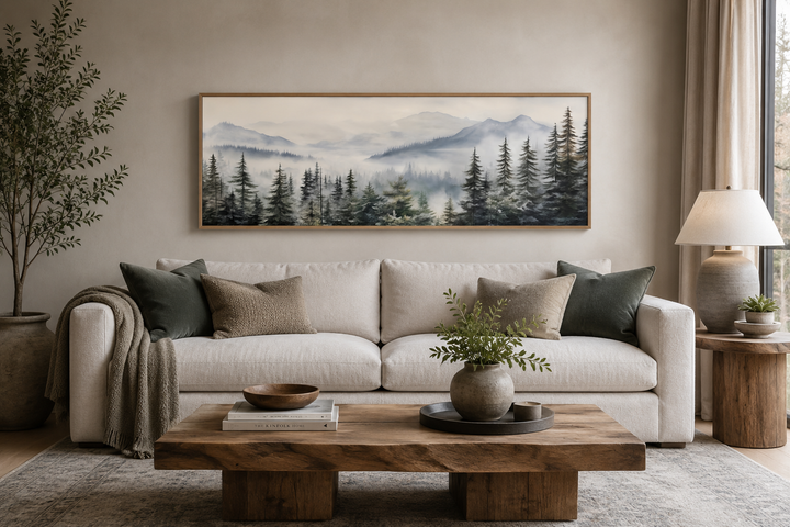 Panoramic foggy forest sage green painting in a wooden frame hanging above a white sofa.