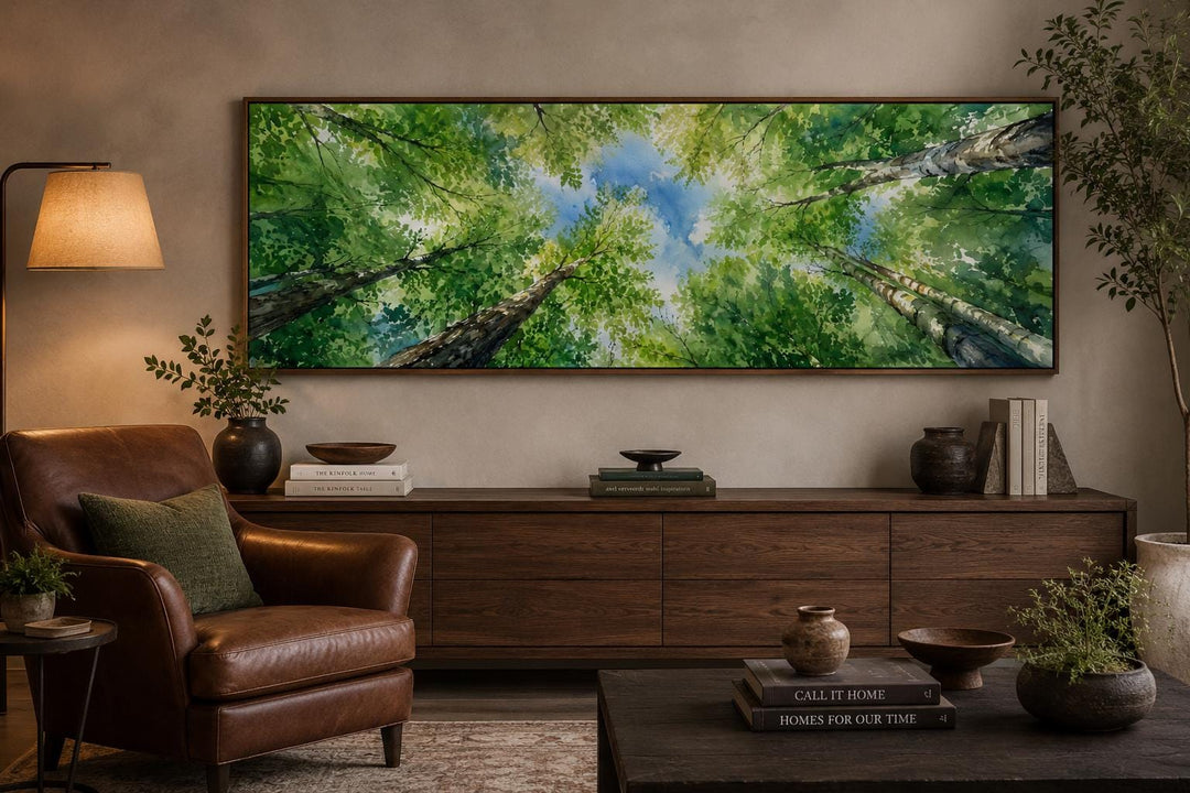 Wide forest canopy wall art with green trees and blue sky above a dark wood sideboard.