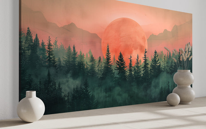 Framed canvas wall art of a pink sun setting over a green forest landscape in a modern room.