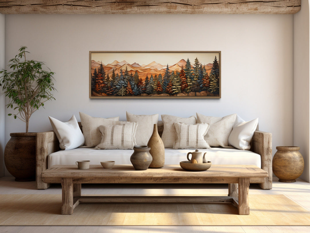 Long horizontal forest canvas wall art with mountains and trees above a rustic sofa.