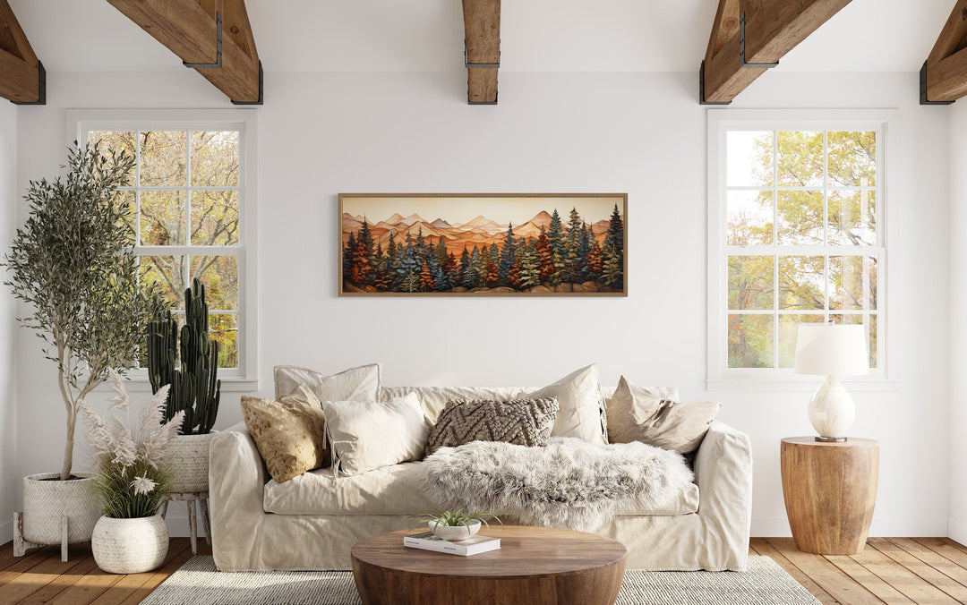 Long horizontal rustic canvas art of a painted forest and mountains above a neutral sofa.