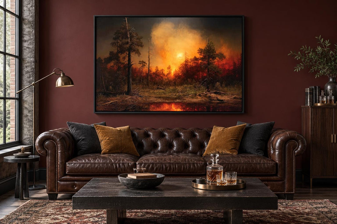 Framed canvas wall art of a forest wildfire with orange flames and smoke above a leather sofa.