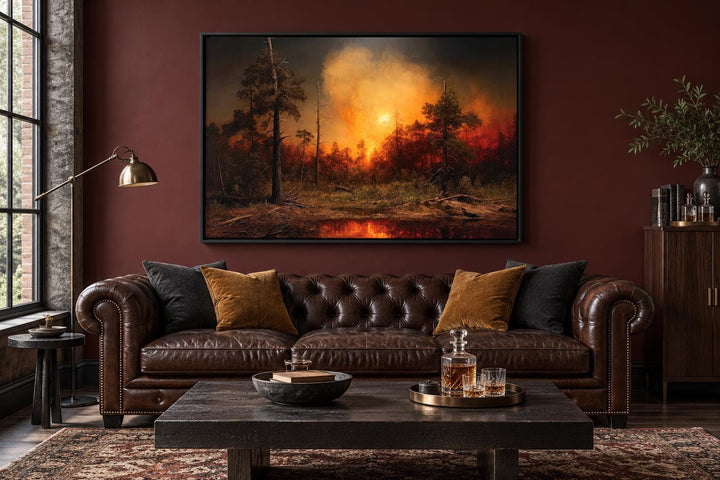 Framed canvas wall art of a forest wildfire with orange flames and smoke above a leather sofa.