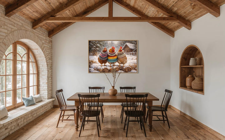Framed canvas print of three chickens in colorful sweaters hanging in a rustic farmhouse dining room.