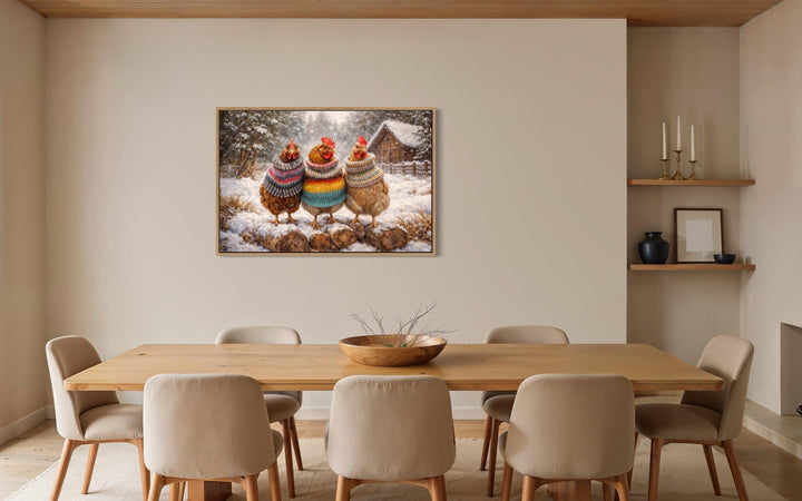 Framed wall art of three chickens in colorful sweaters in a snowy scene above a dining table.