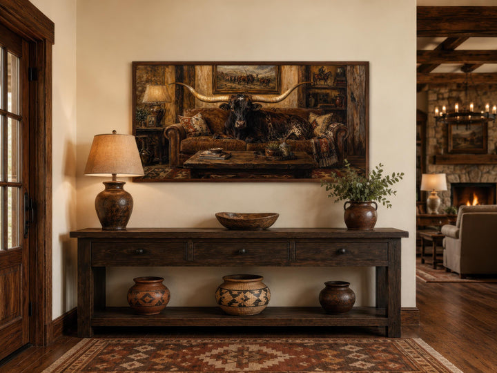 Framed canvas art of a Texas Longhorn bull lounging on a leather sofa in a rustic ranch interior.