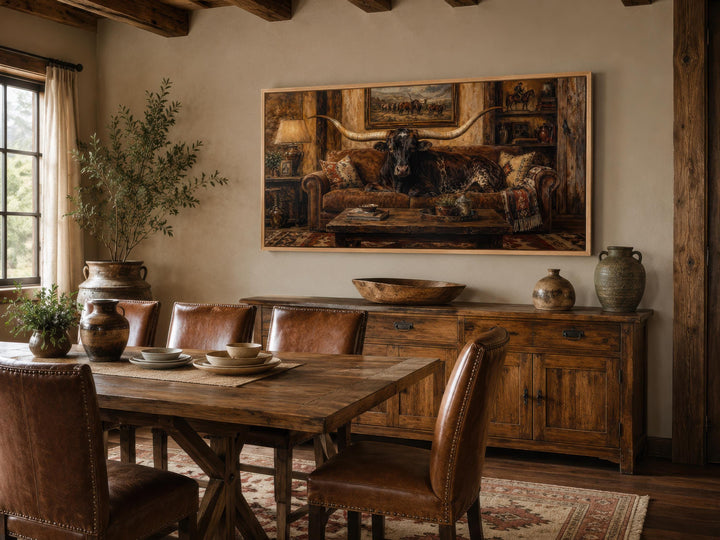Framed canvas art of a Texas Longhorn bull lounging on a couch in a rustic ranch dining room.