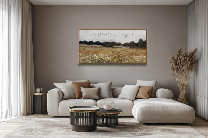 Horizontal landscape wall art of a wildflower field with scripture text above a modern beige sofa.
