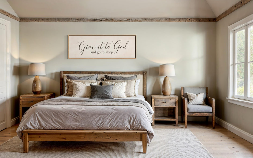 Give it to God and Go to Sleep long horizontal canvas sign hanging above a bed in a neutral bedroom.