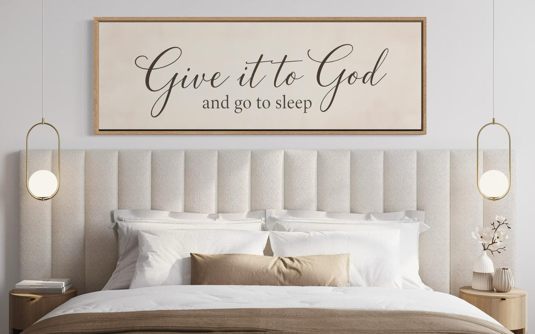 Give it to God and Go to Sleep long horizontal canvas sign in a wood frame above a modern bed.