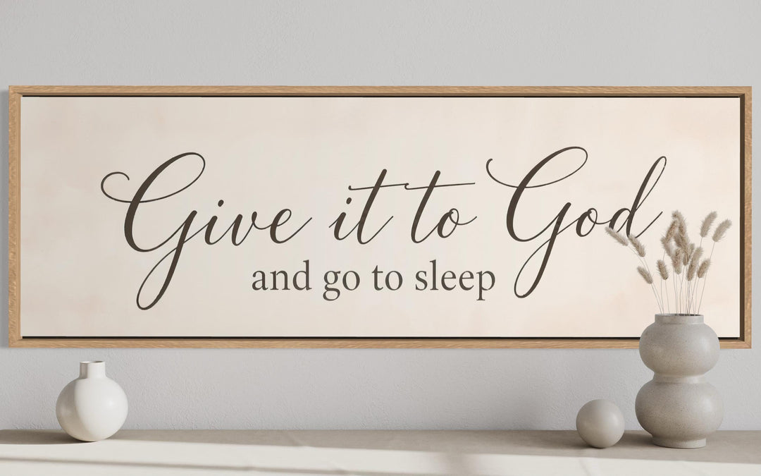 Give it to God and Go to Sleep long horizontal wall art sign in a wood frame above a console table.