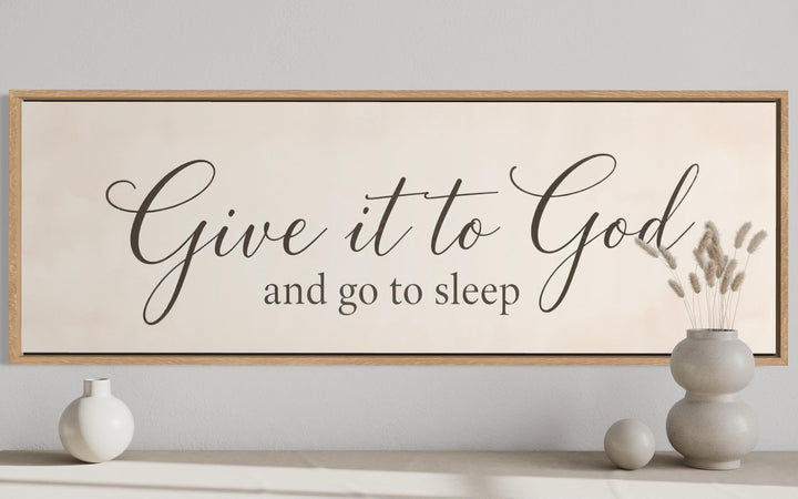 Give it to God and Go to Sleep long horizontal wall art sign in a wood frame above a console table.
