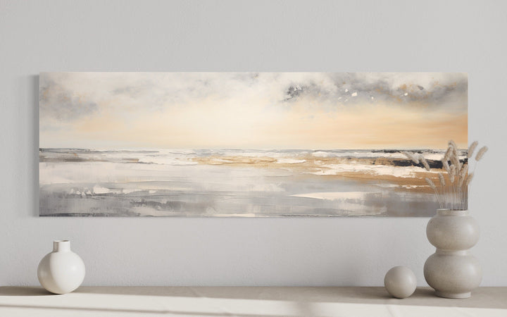 Gold and silver abstract beach sunset panoramic wall art above a minimalist shelf with vases.