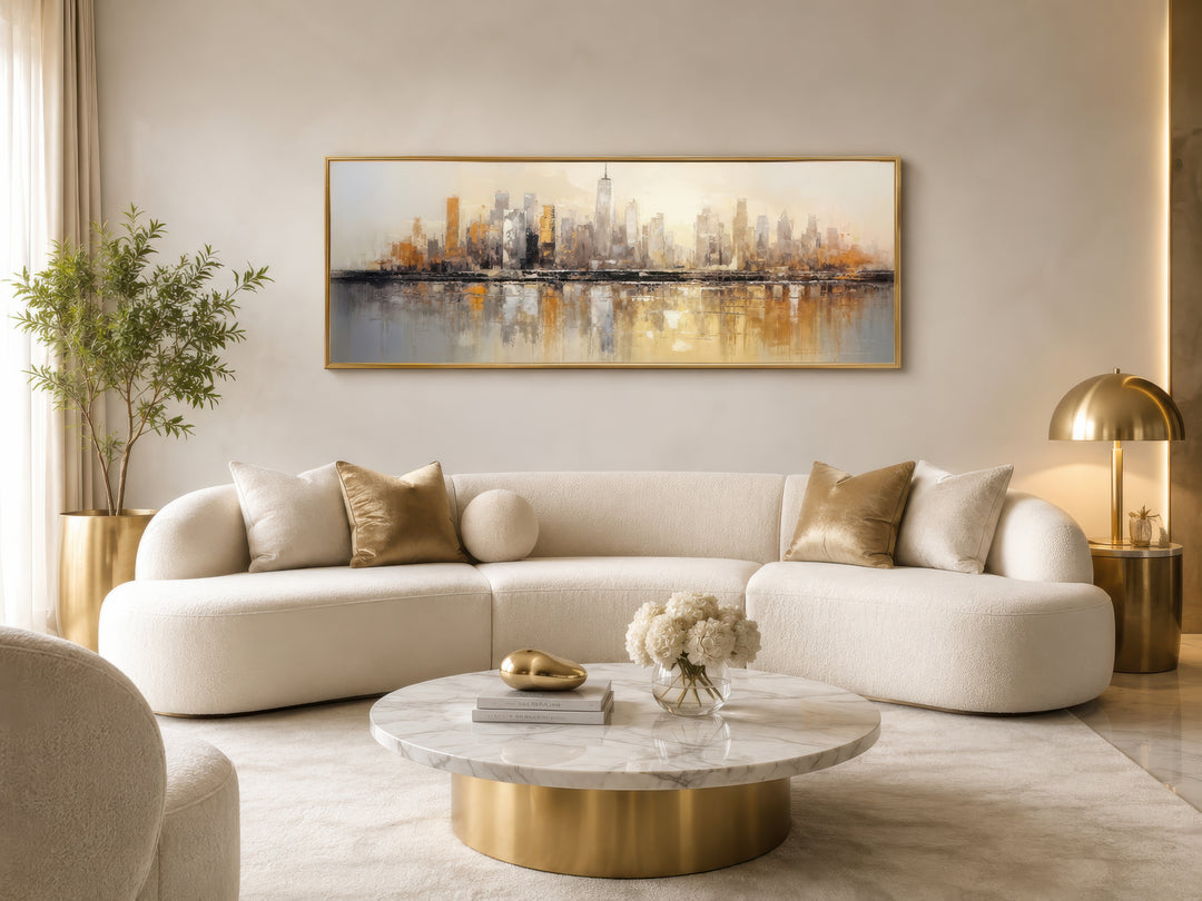 Gold and silver abstract New York City skyline horizontal wall art above a white curved sofa.
