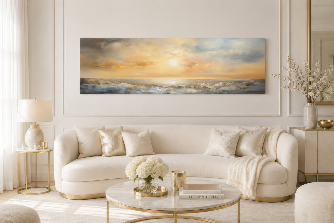 A long horizontal abstract painting of a golden ocean sunset hangs above a modern white sofa.