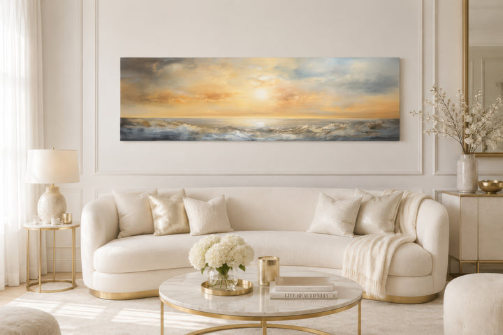 A long horizontal abstract painting of a golden ocean sunset hangs above a modern white sofa.