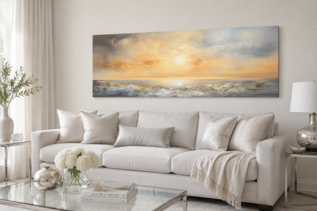 A long horizontal abstract painting of a golden ocean sunset hangs above a white sofa.
