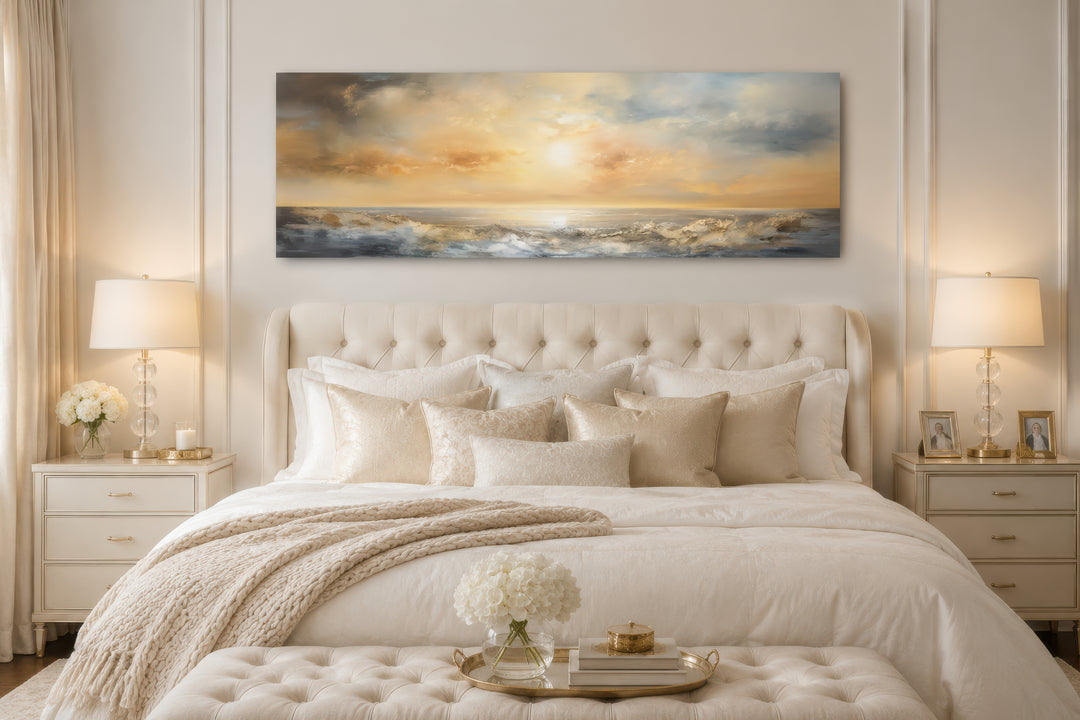 Long horizontal abstract ocean sunset wall art in gold and silver tones hanging over a bed.