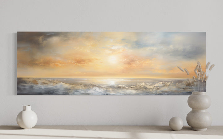 Long horizontal abstract painting of a gold and silver ocean sunset hanging on a neutral wall.