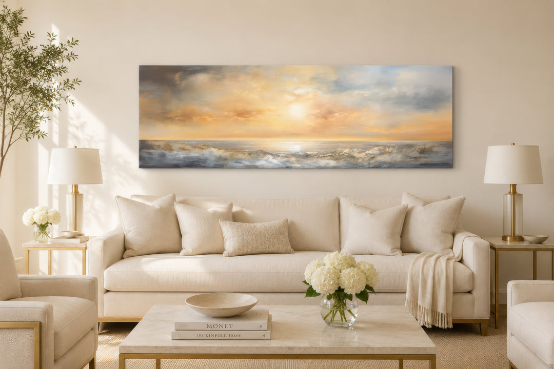 A long horizontal abstract painting of a gold and silver ocean sunset hangs over a neutral sofa.