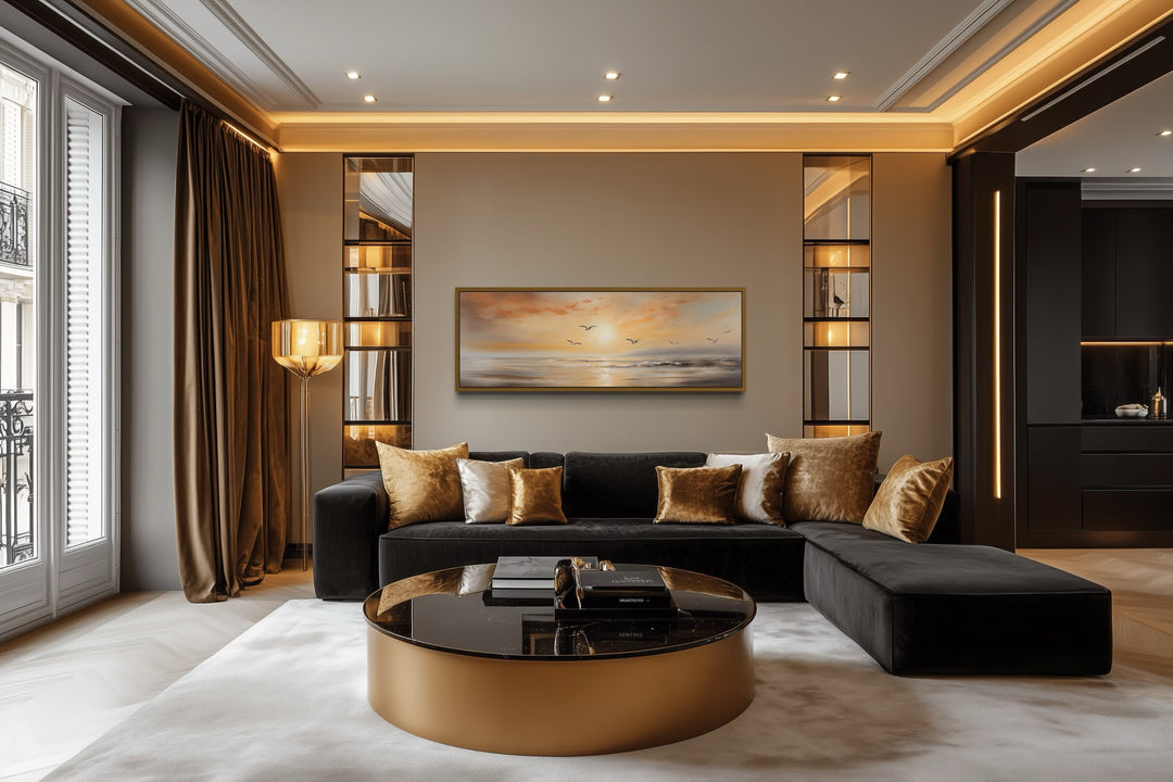 Narrow horizontal wall art of a gold and silver beach sunset with birds above a black sofa.