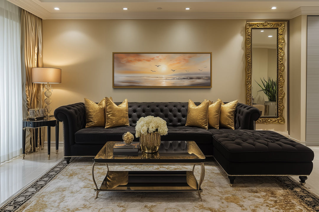 Narrow horizontal wall art of a gold and silver beach sunset with birds above a black sofa.