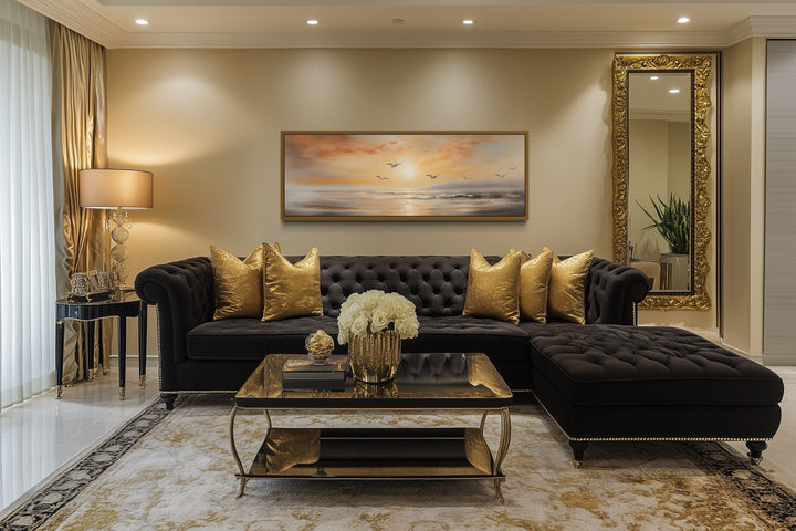 Narrow horizontal wall art of a gold and silver beach sunset with birds above a black sofa.