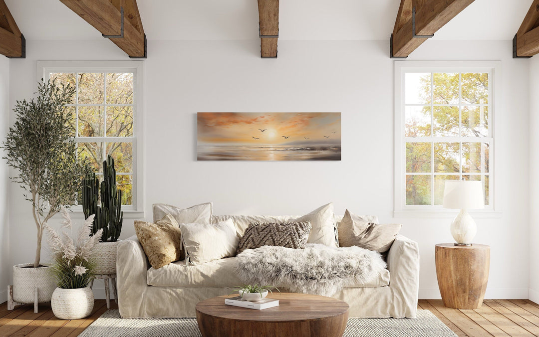 Gold and silver beach sunset seascape with birds narrow horizontal wall art above a beige sofa.