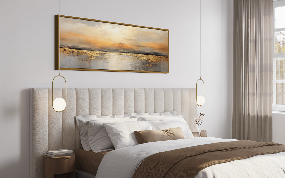 Gold and silver ocean sunset horizontal wall art hanging above a modern upholstered bed.
