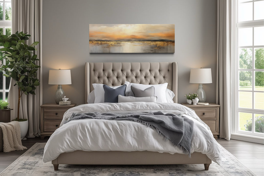 Gold and silver ocean sunset horizontal wall art hanging above a tufted bed in a neutral bedroom.