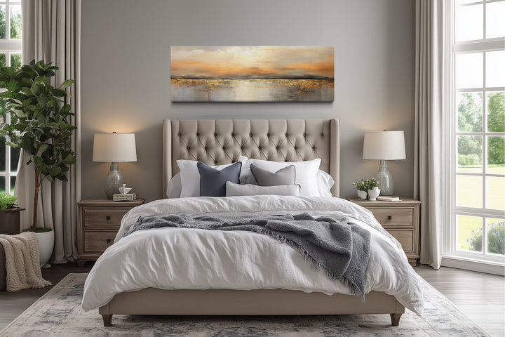Gold and silver ocean sunset horizontal wall art hanging above a tufted bed in a neutral bedroom.