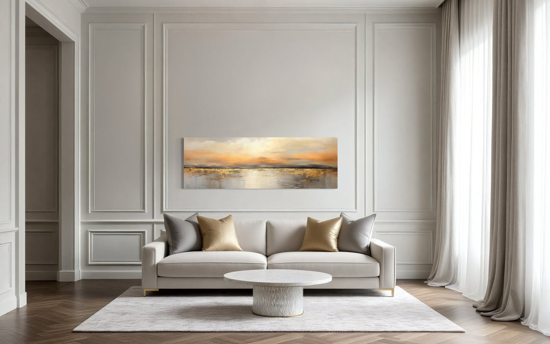 Gold and silver ocean sunset horizontal wall art hanging above a white sofa in a modern room.