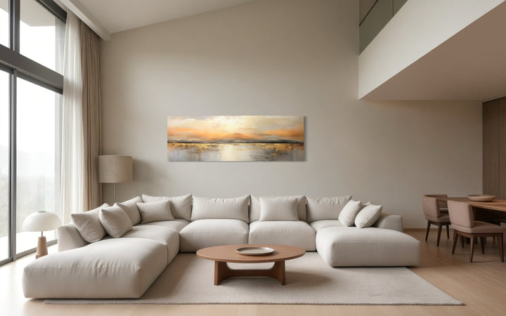 Gold and silver ocean sunset long horizontal wall art hanging above a large white sectional sofa.