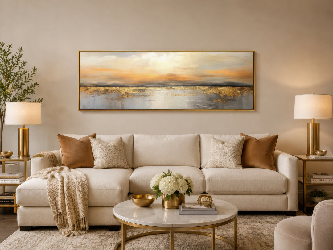 Gold and silver ocean sunset long horizontal wall art in a gold frame above a cream sofa.