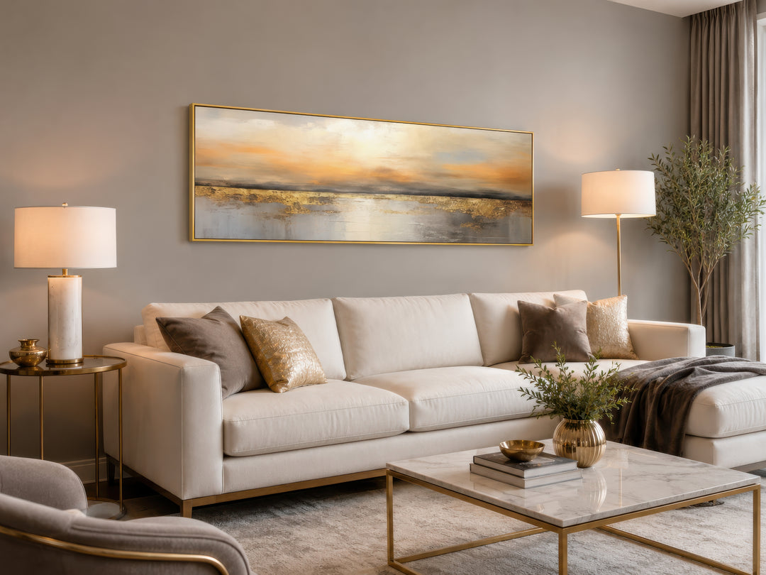 Long horizontal gold and silver abstract ocean sunset wall art hanging above a white sofa.